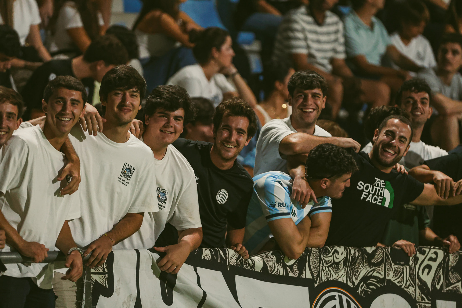 Jóvenes aficionados sonriendo junto a la valla de noche